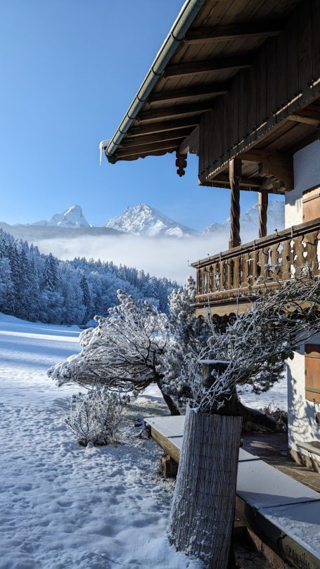 Berglandschaft mit schneebedecktem Haus und gefrorenen Bäumen im Vordergrund.