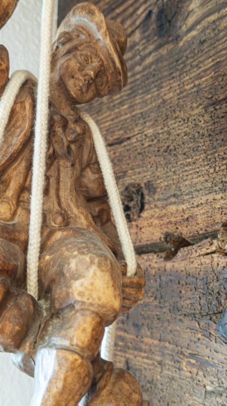 Eine geschnitzte Holzfigur, die an einem Seil hängt, vor einer rustikalen Holzoberfläche.