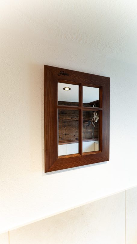 Holzrahmen mit Fenstergitter, reflektierendes Glas und eine schlichte Wand dahinter.