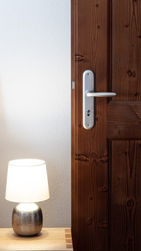 Ein Holzteil einer Tür mit einem modernen Türgriff und einer kleinen Lampe daneben.
