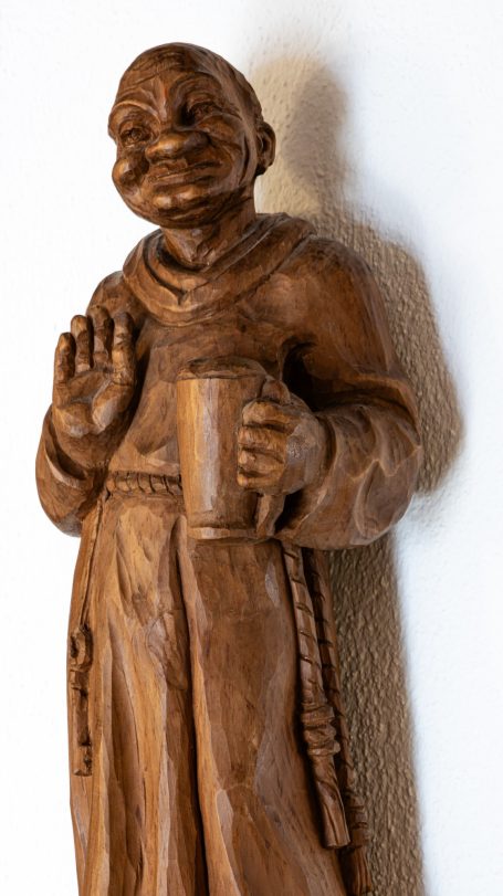 Eine hölzerne Statue eines Mönchs, der einen Becher hält und freundlich winkt.