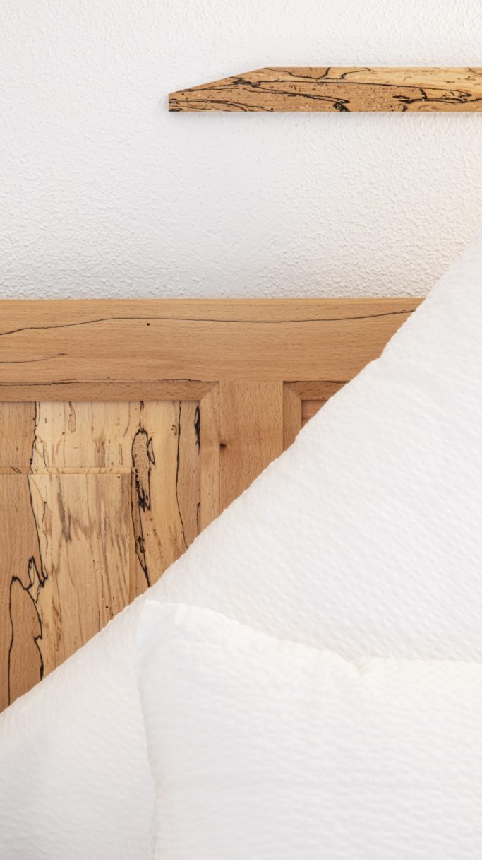Holzkopfteil eines Bettes mit kissenbedecktem Kopfkissen und schlichter Wand.