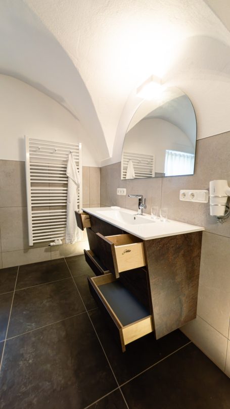 Modernes Badezimmer mit Waschbecken, Spiegel und einem niedrigen Möbelstück.