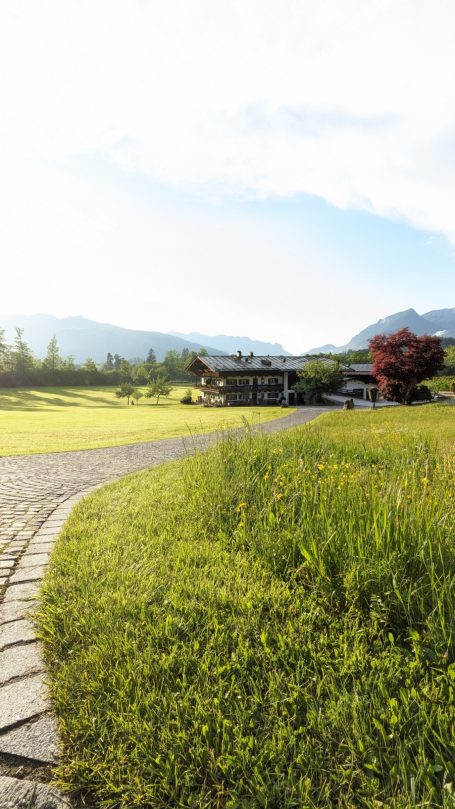 Landschaft mit grünem Gras, einem Weg und einem traditionellen Gebäude im Hintergrund.