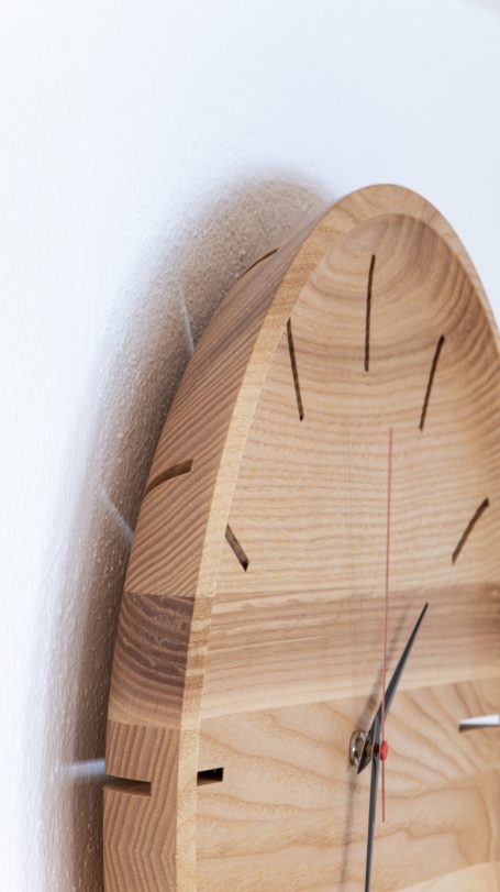 Holzuhr mit geschwungener Form und minimalistischen Stundenmarkierungen.