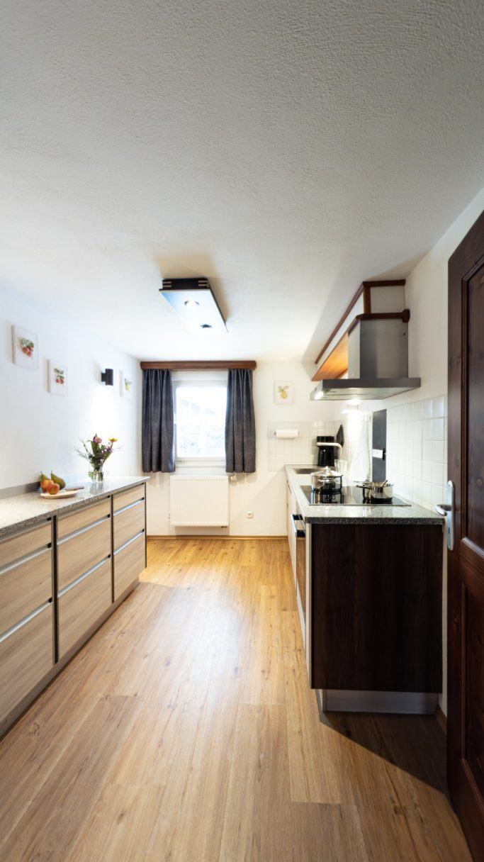 Moderne Küche mit Holzfußboden, Fenster und Kochbereich in hellen Farbtönen.