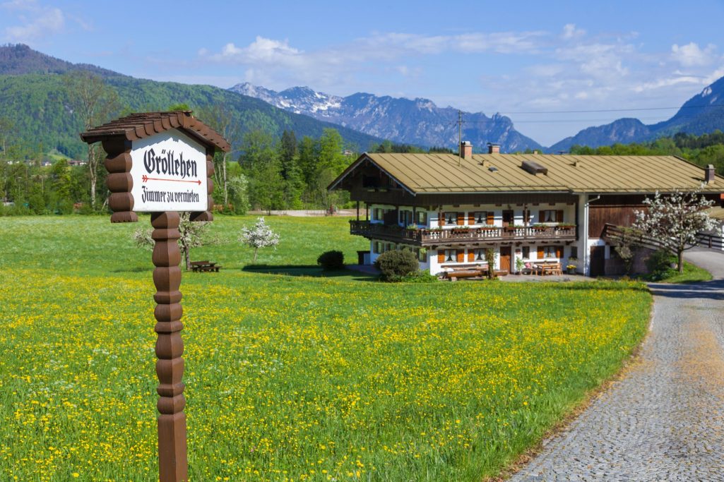 Traditionelles alpenländisches Haus mit blühendem Gelände und Bergen im Hintergrund.