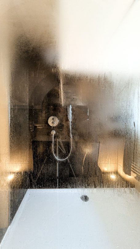 Dampfe Dusche mit modernen Armaturen und sanfter Beleuchtung im Hintergrund.