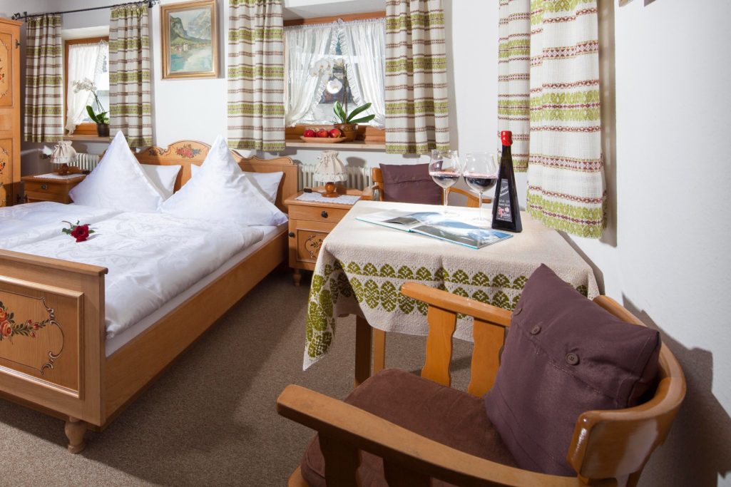 Gemütliches Zimmer mit Doppelbett, Tisch und Stuhl, dekoriert mit Pflanzen und Vorhängen.