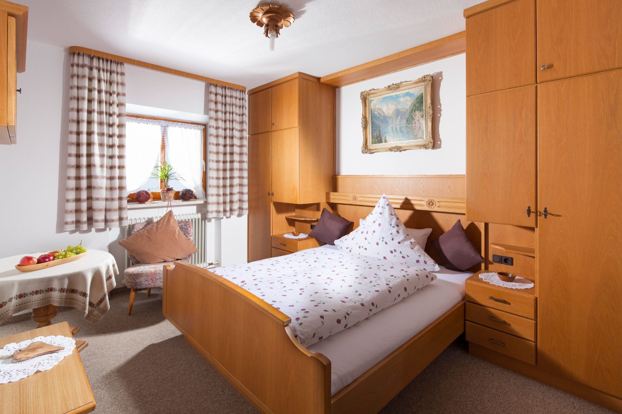 Helles Zimmer mit Holzmöbeln, Doppelbett und einem kleinen Tisch neben dem Fenster.